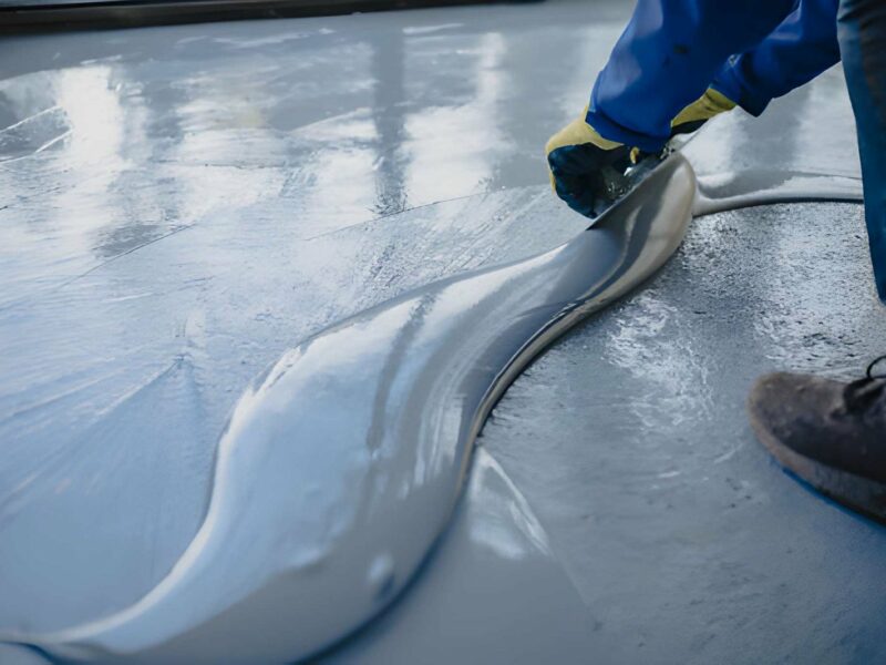 Contractor using a squeegee to spread thick gray liquid epoxy coating across a prepared concrete floor